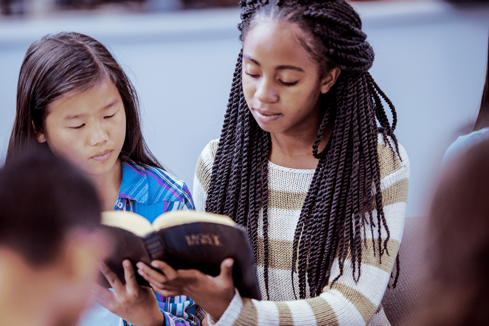 Two young girls huddle together to read a book