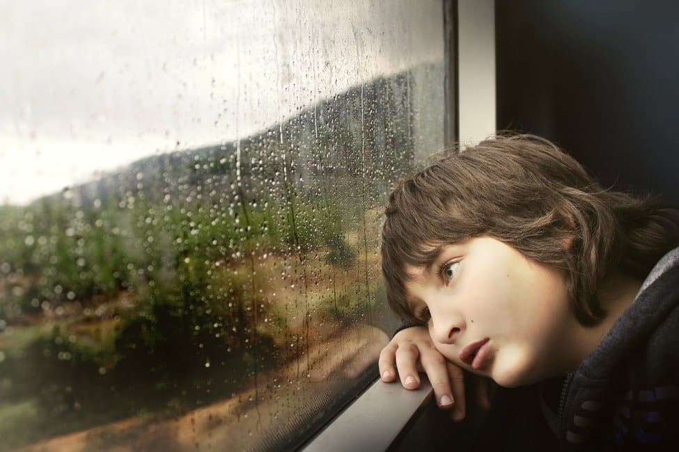 Young boy looking out a rainy window