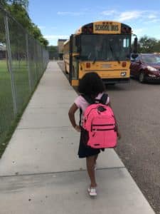 Student with pink backpack walking toward bus