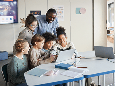 A teacher and five children looking at a laptop together