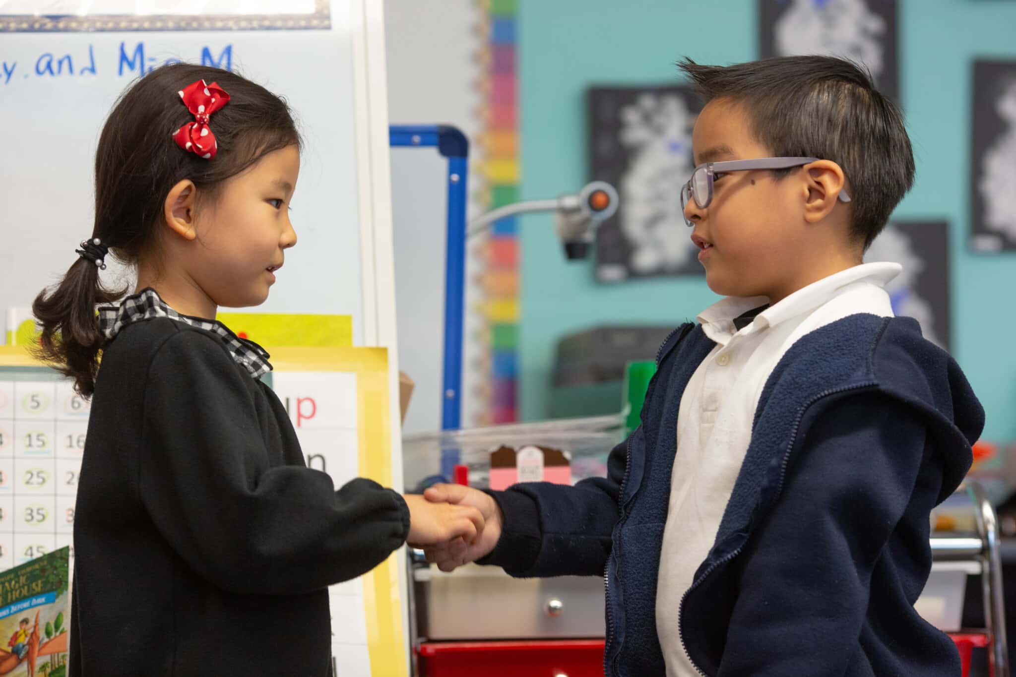 A girl child and boy child shaking hands in their classroom