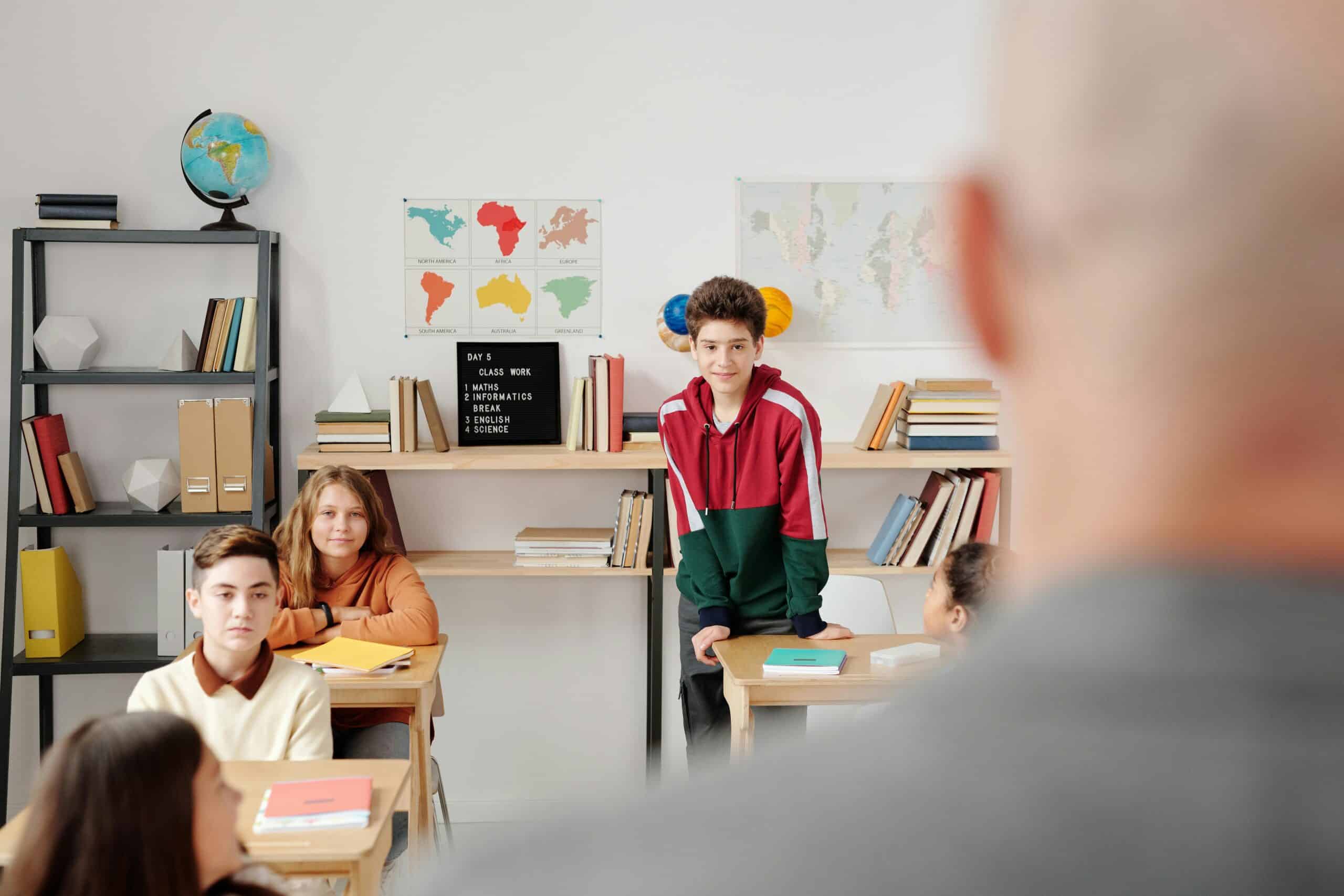 Student in red sweater getting up from his desk with teacher in the foreground