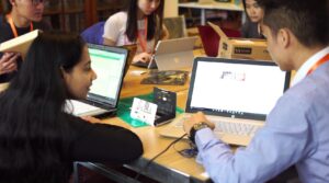 A student and a teacher sitting at a desk and looking at a laptop.